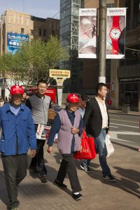 Touristes chinois reconnaissable à leurs casquettes rouges dans les rues de Shanghai qui marchent sous une publicité de Swatch les fameuses montres Suisses.